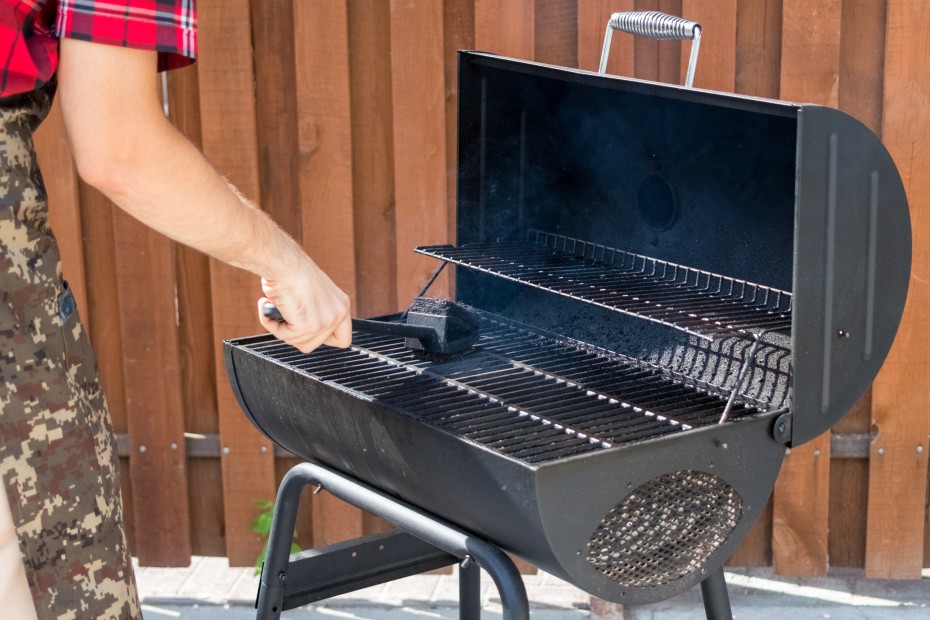 A man cleans the barbecue with a wire brush.