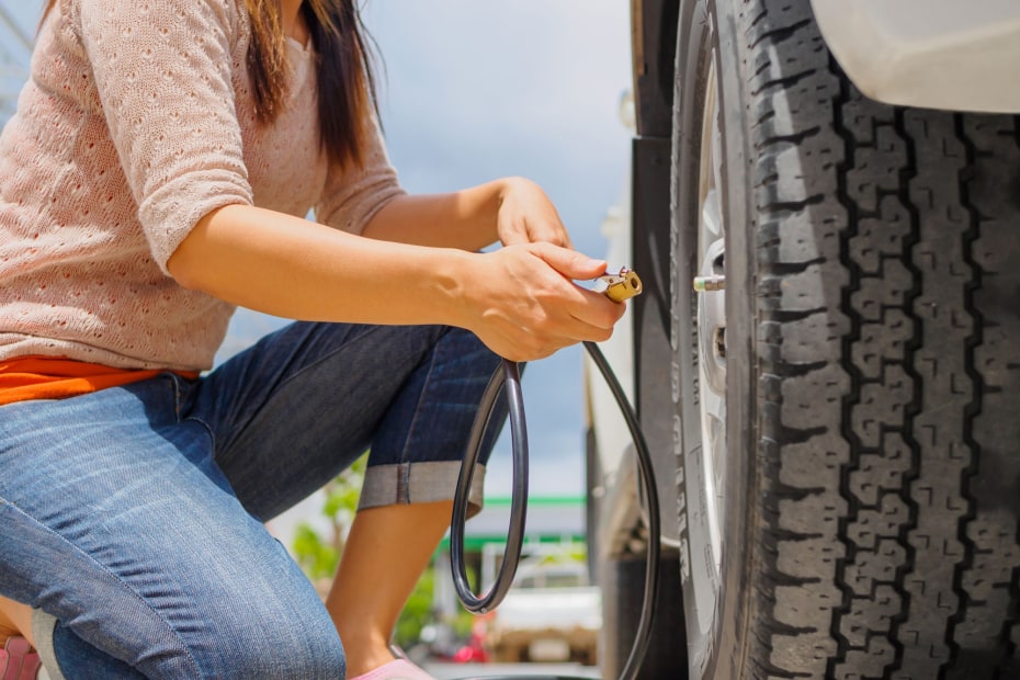 A woman fills her car tire with air at a gas station.