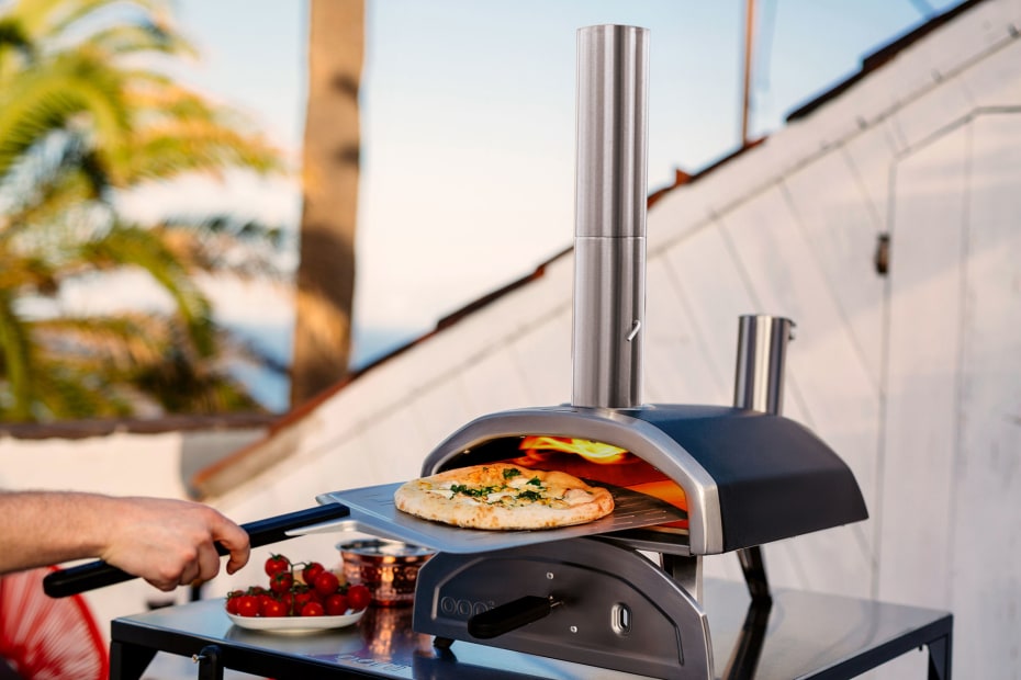 A person removes a pizza from their countertop outdoor pizza oven.