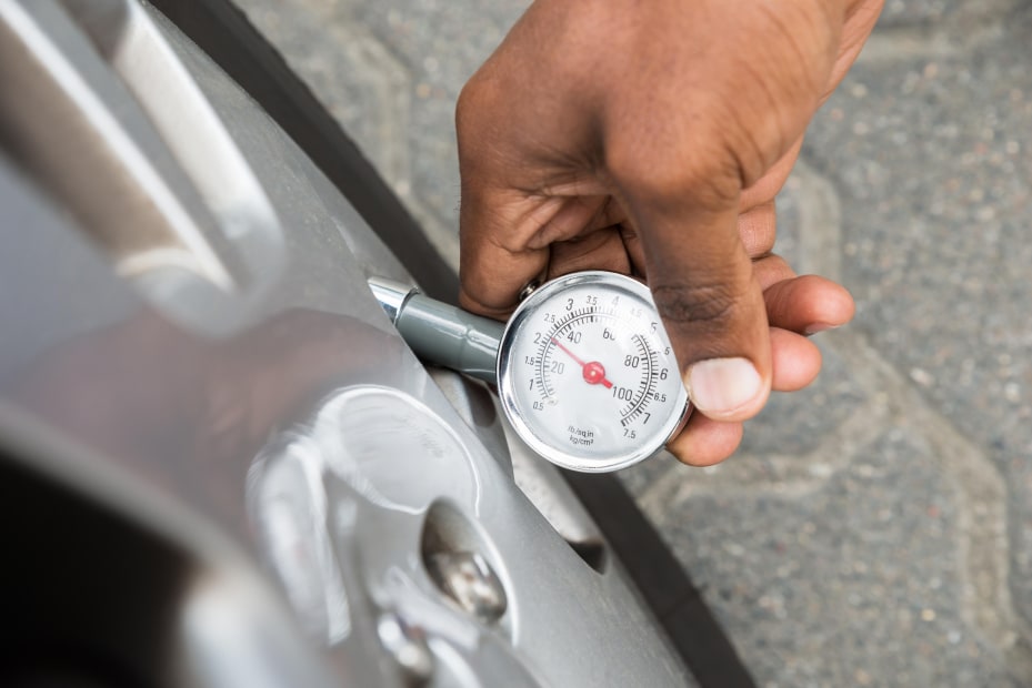 A driver uses a tire pressure gauge outside.