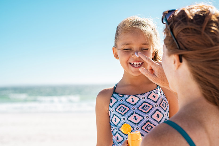 A woman puts sunscreen on her child's face.