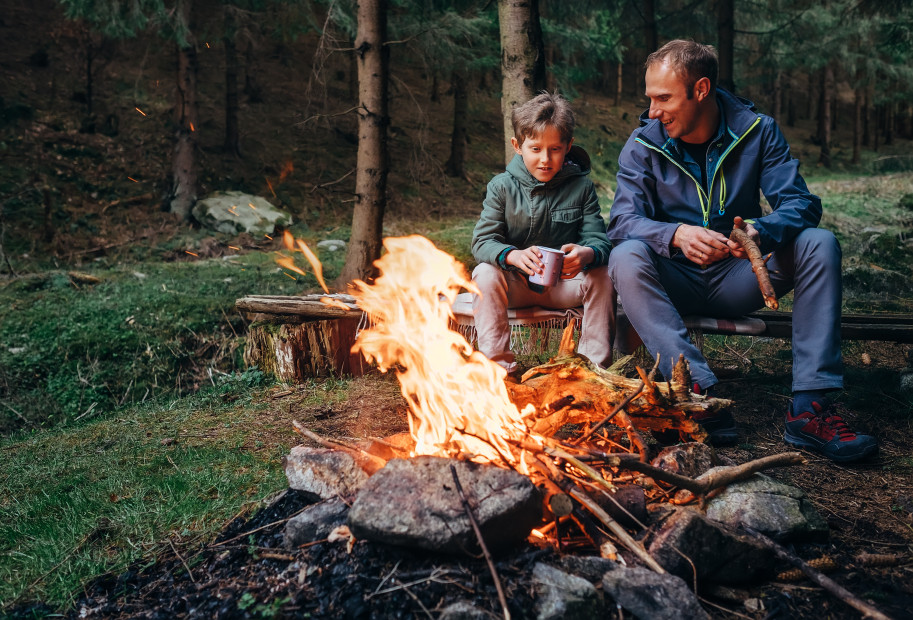A father and son sit around a campfire.