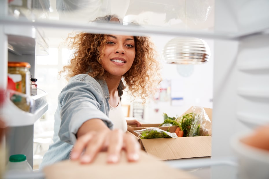 A woman puts groceries away in the refridgerator.