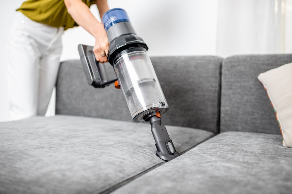 A person vacuums their gray sofa.