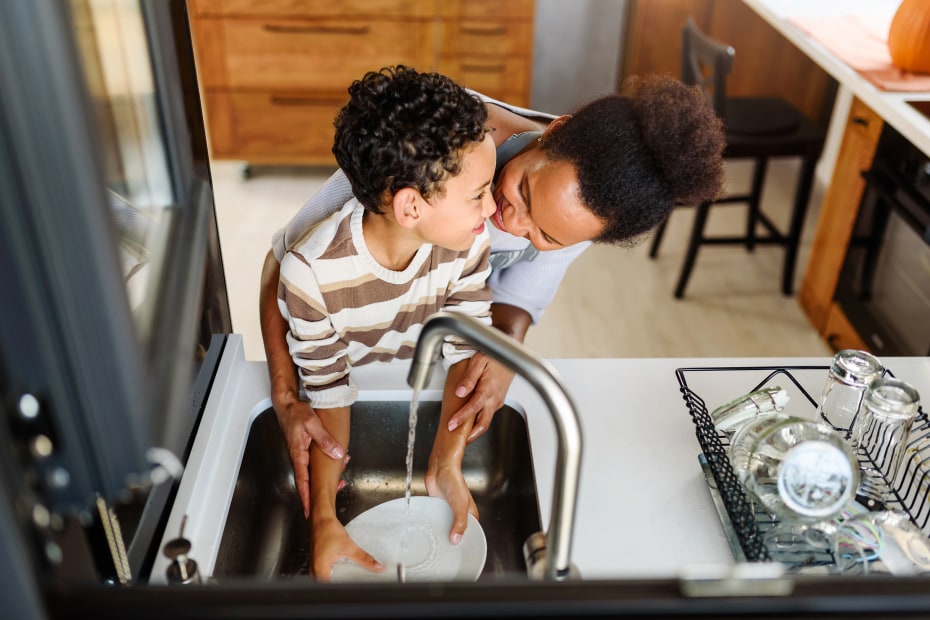 A son and his mom do the dishes in a modern black sink.