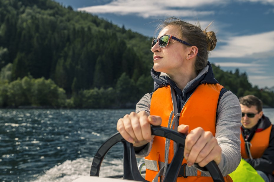 A woman drives a boat in a life jacket.