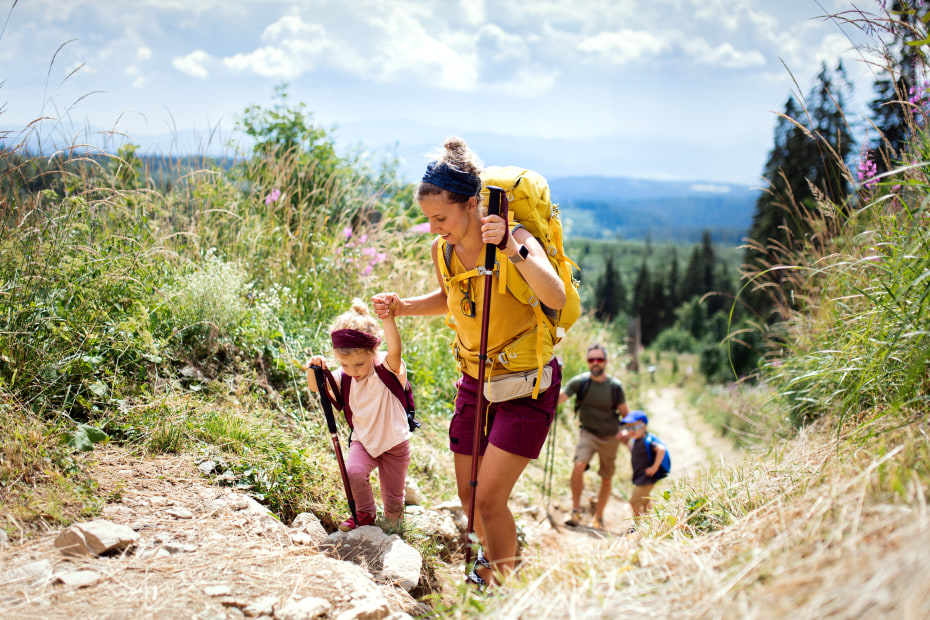 A mom holds her young daughter's hand to help her up a hiking trail.