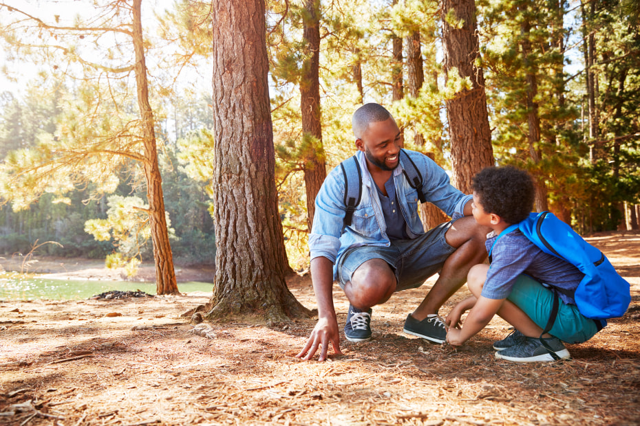 A father and son look for animal tracks on a dirt hiking trail.