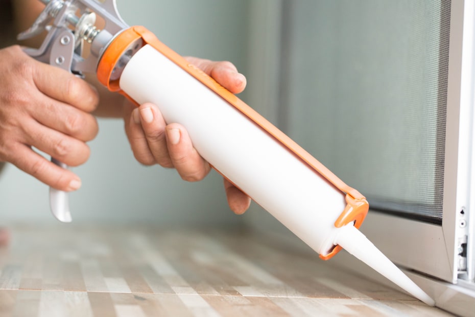 A homeowner caulks the base of their sliding door.