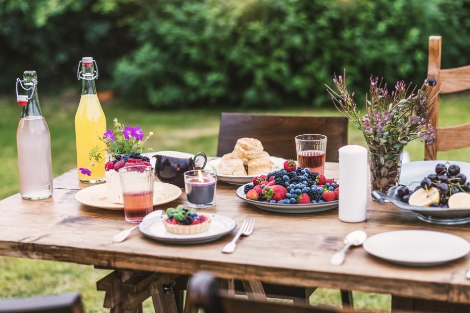 An outdoor dining table set with berry tarts and juice.