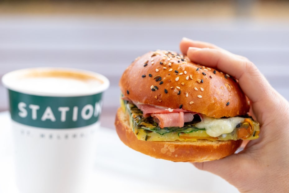 A person holds a breakfast sandwich with a latte in the background.