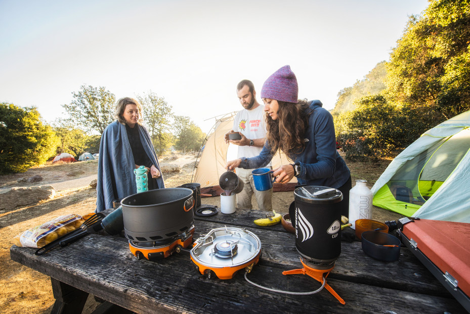 Friends make coffee and breakfast on a camping stove.