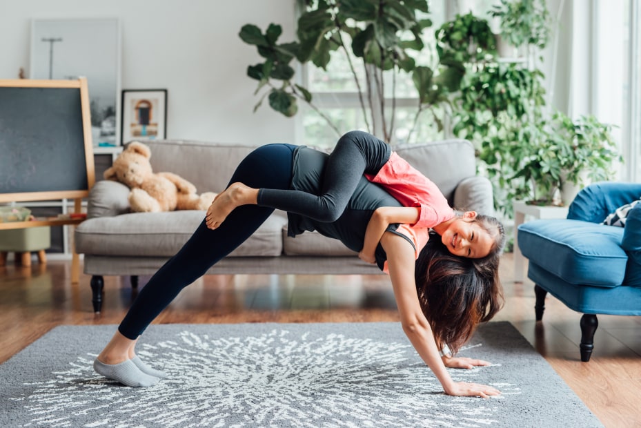 A mom and her daughter do yoga together in the living room.