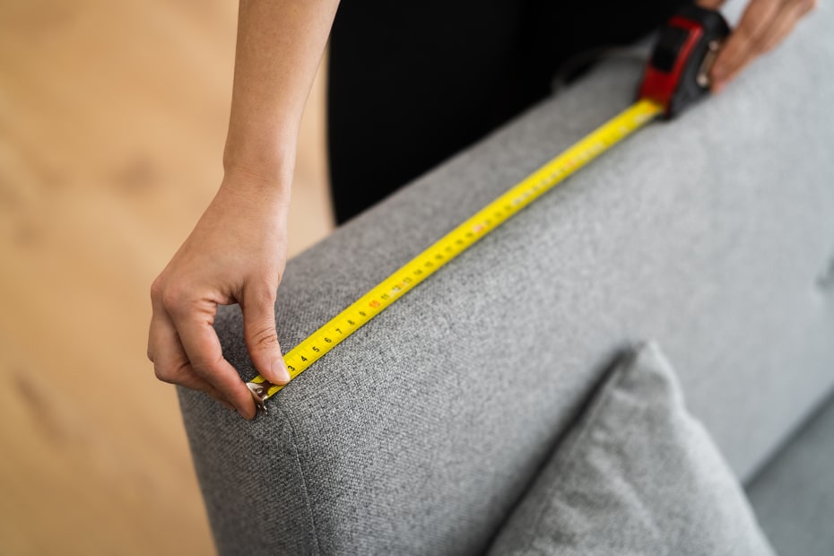A person measures the length of a used sofa.