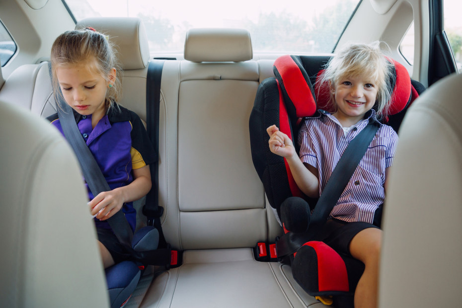 Two girls sit in the backseat in booster seats.