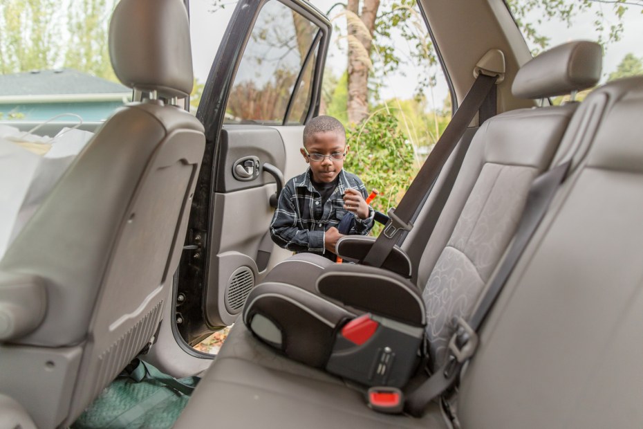 A young boy gets into his booster seat in the backset of a sedan.