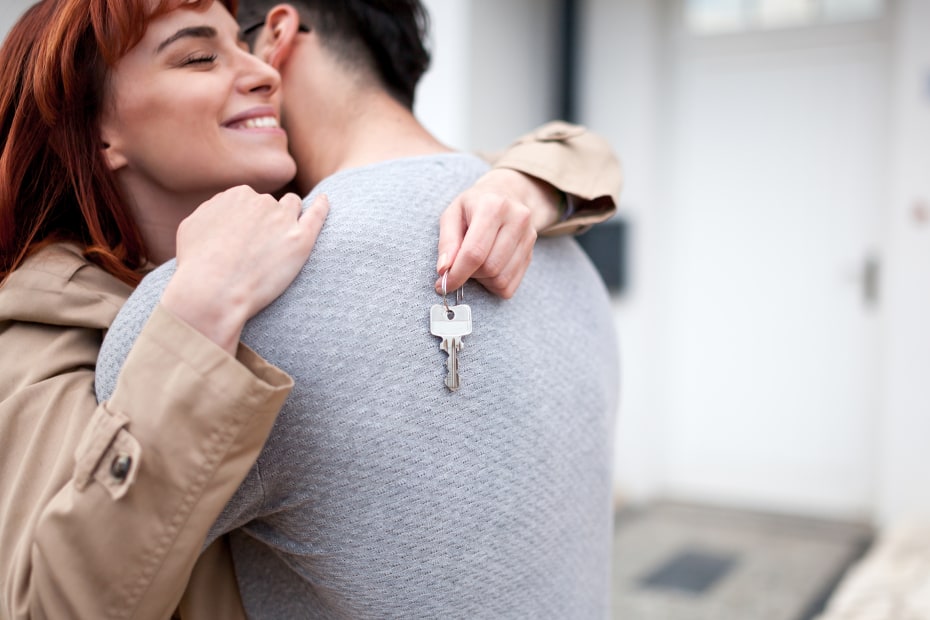 A couple hug while holding the keys to their new home.