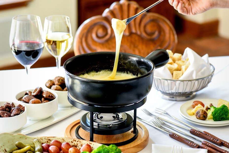 A person dips a piece of bread into the Goldener Hirsch Restaurant’s Fondue.