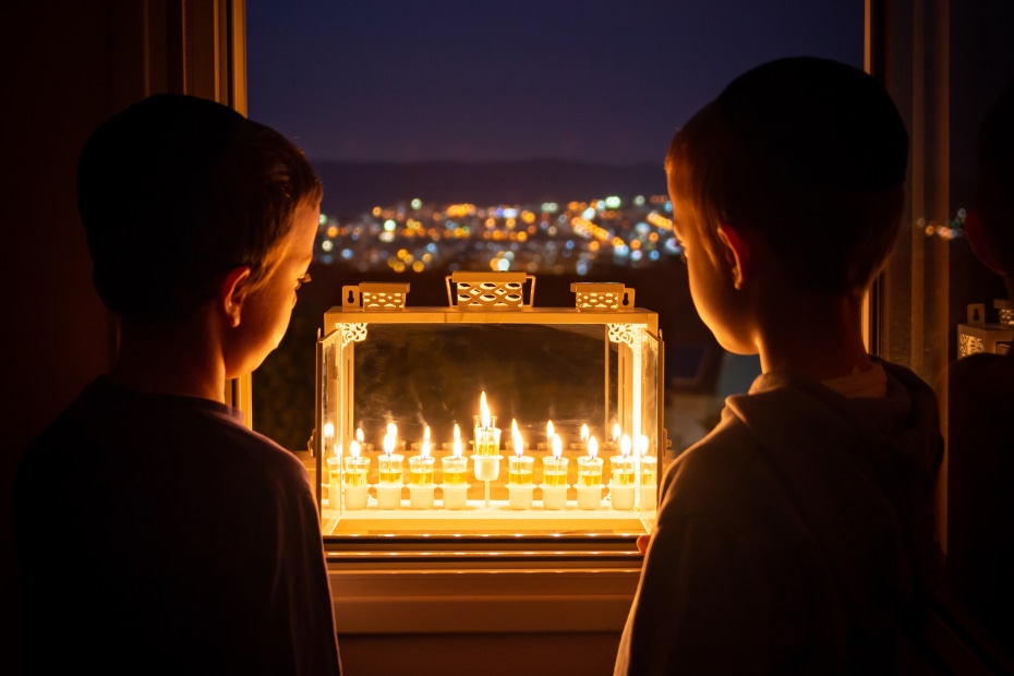 Two boys look at a menorah in a window.