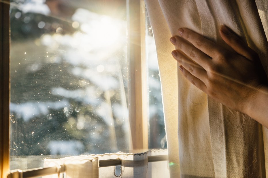 A person pulls back their curtains to let the sunlight warm up the house.