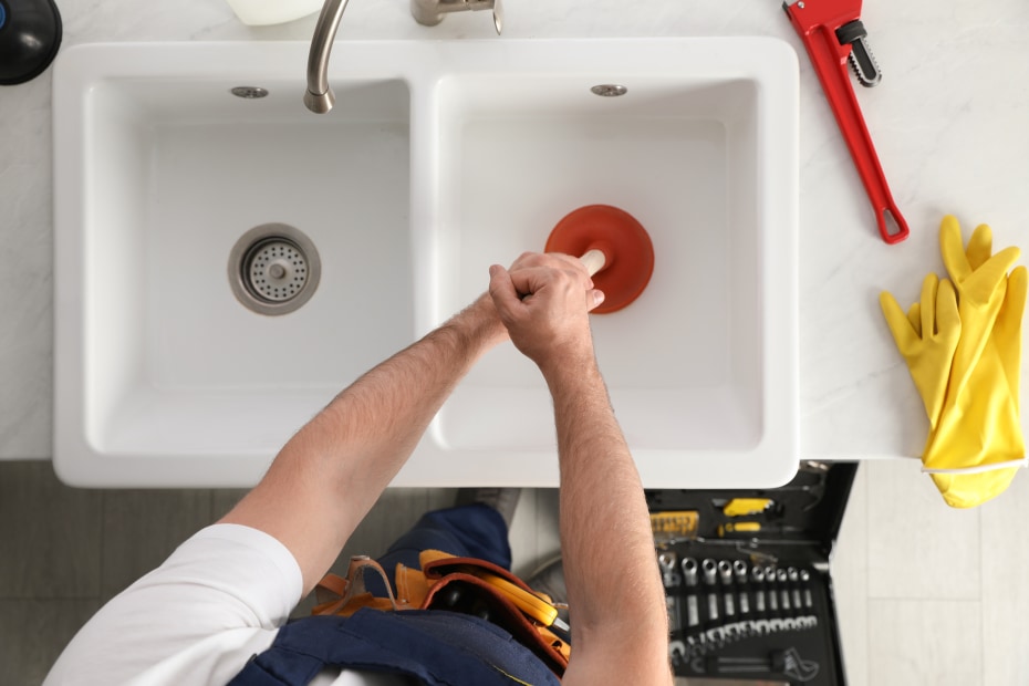 A plumber uses a plunger to drain a clogged kitchen sink.