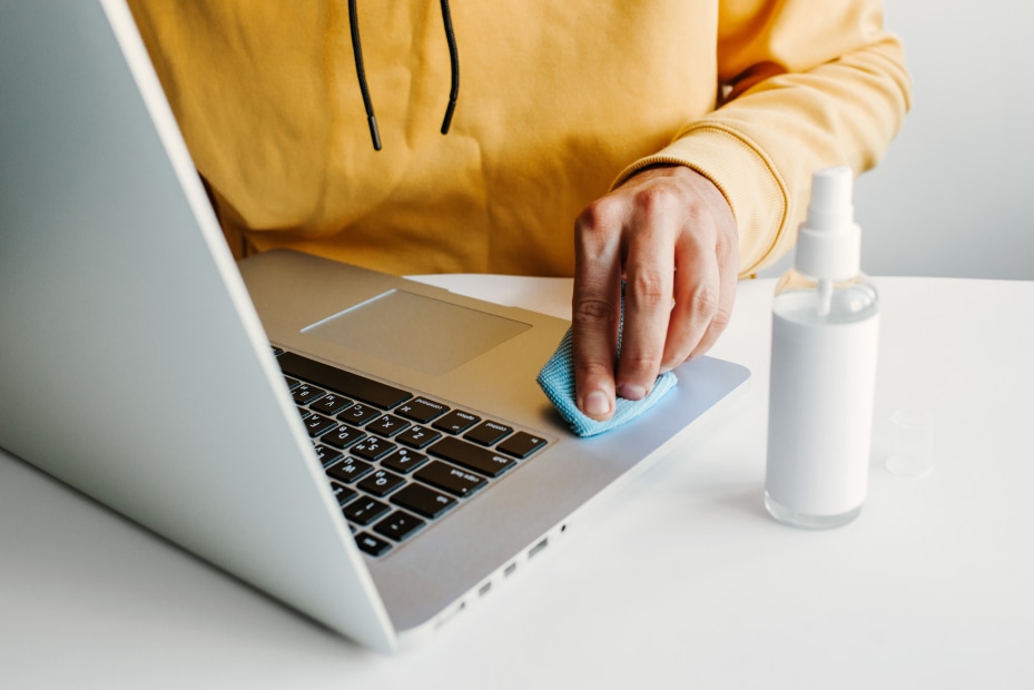 A person cleans their laptop with a microfiber cloth.