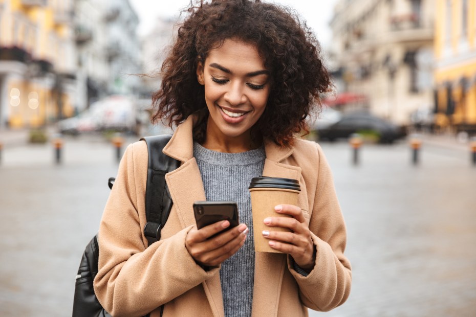 A woman walks with her phone and a coffee in her hands.