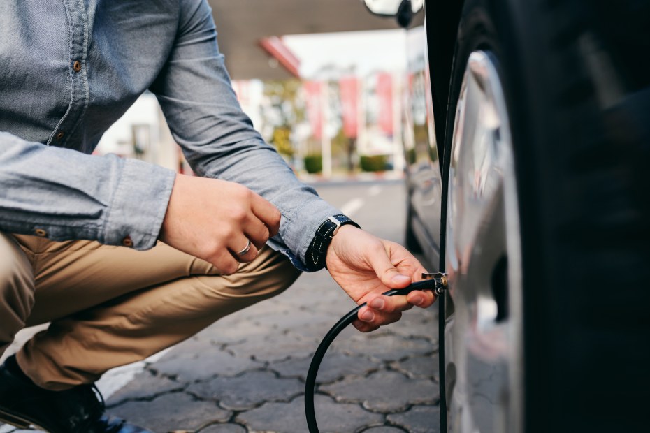 A driver fills his car tire with compressed air.