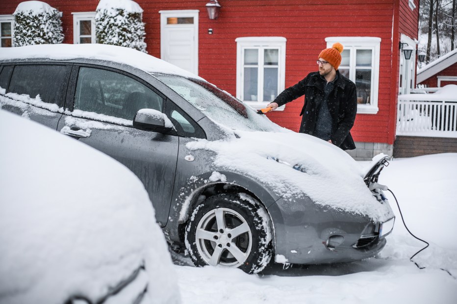 A driver removes snow and ice from their electric car.