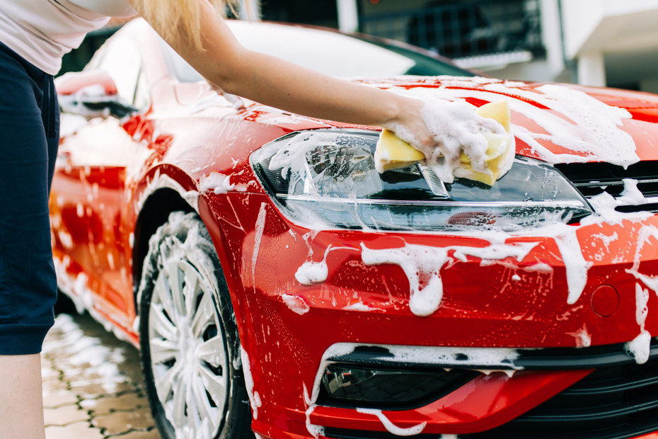 A woman washes her red sedan.