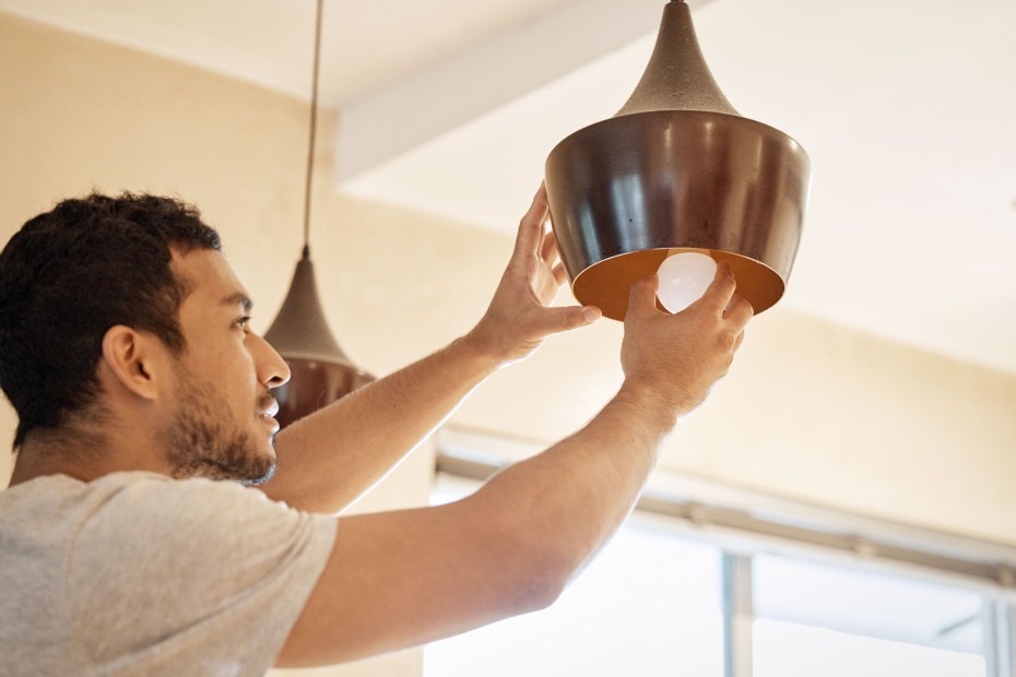 A man replaces a light bulb in a pendant light.