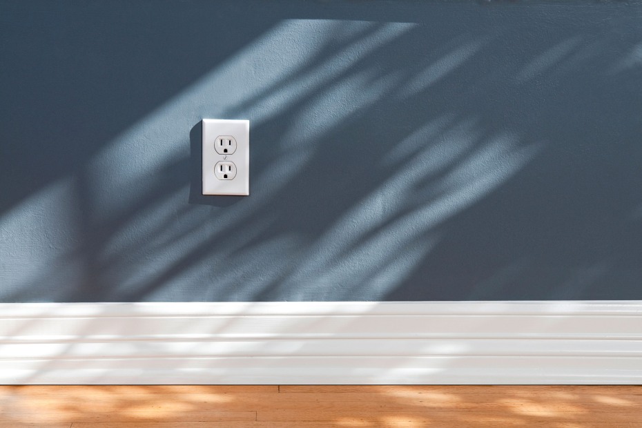 A white electrical outlet against a blue living room wall.