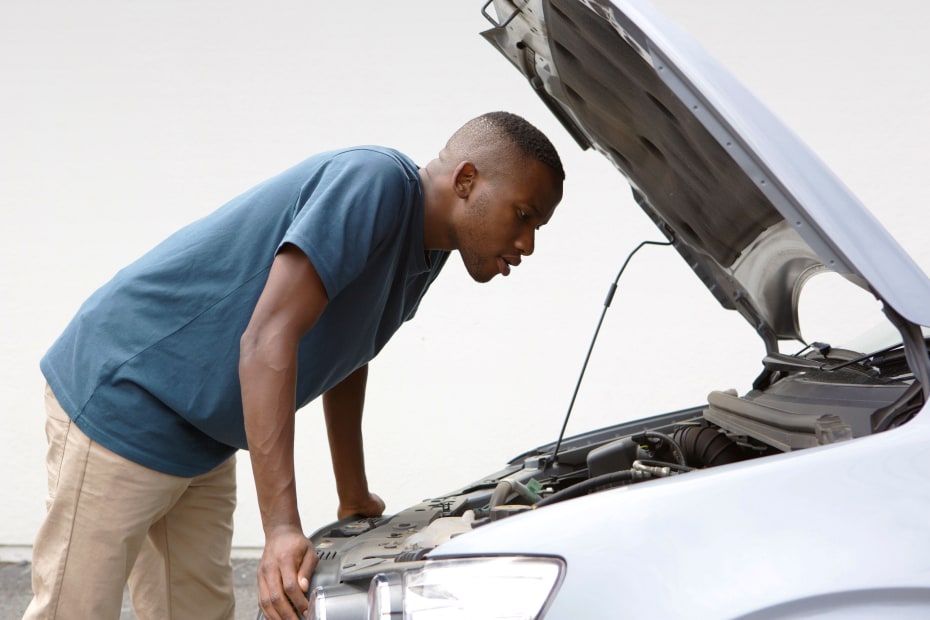 A young man looks under the hood of his car.