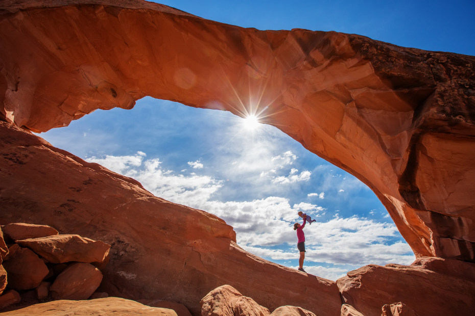A woman holds her baby up underneath Skyline Arch in Arches National Park.