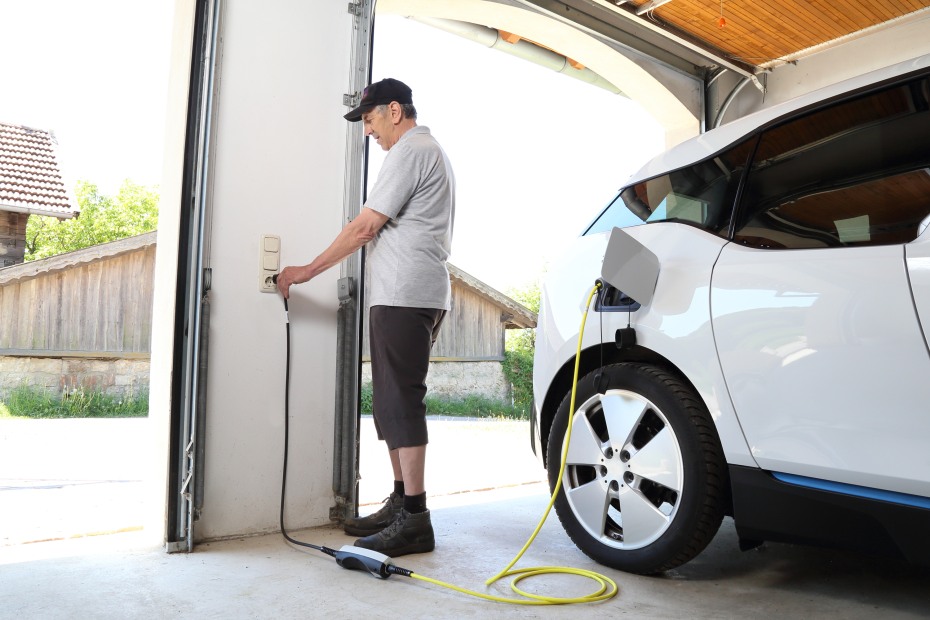 A man plugs his EV into an outlet in his garage to trickle charge.