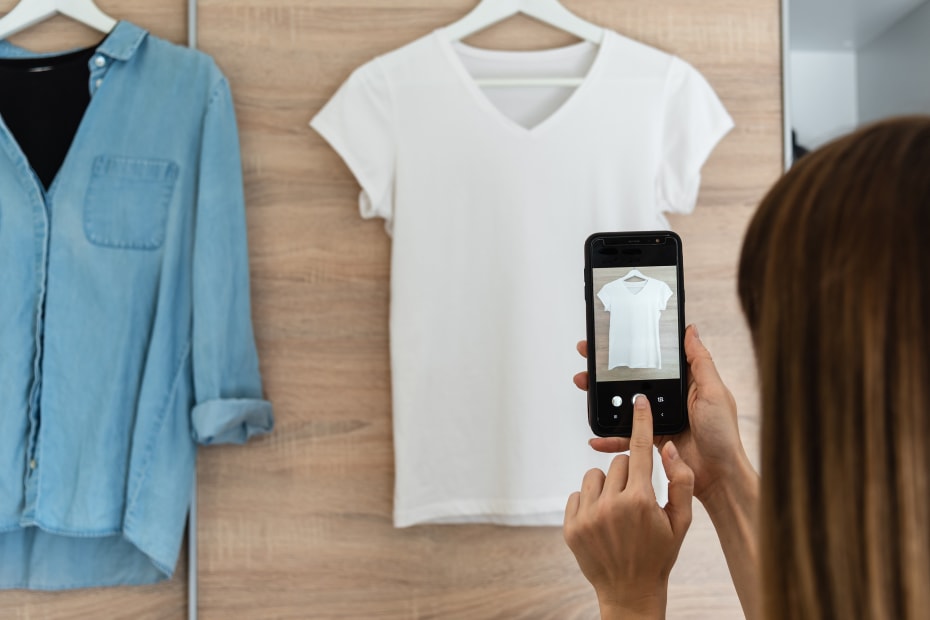 A woman takes a picture of used clothes to sell them.