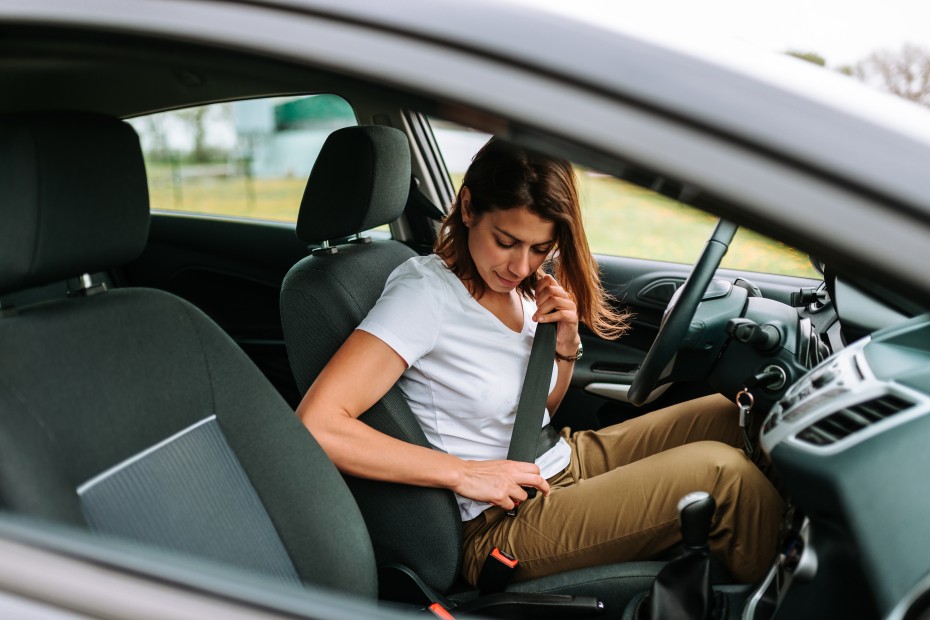 A woman puts on her seatbelt before driving.