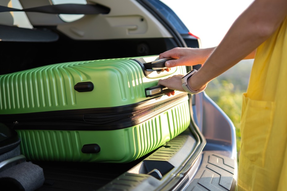 A woman puts a green suitcase into the back of an SUV.