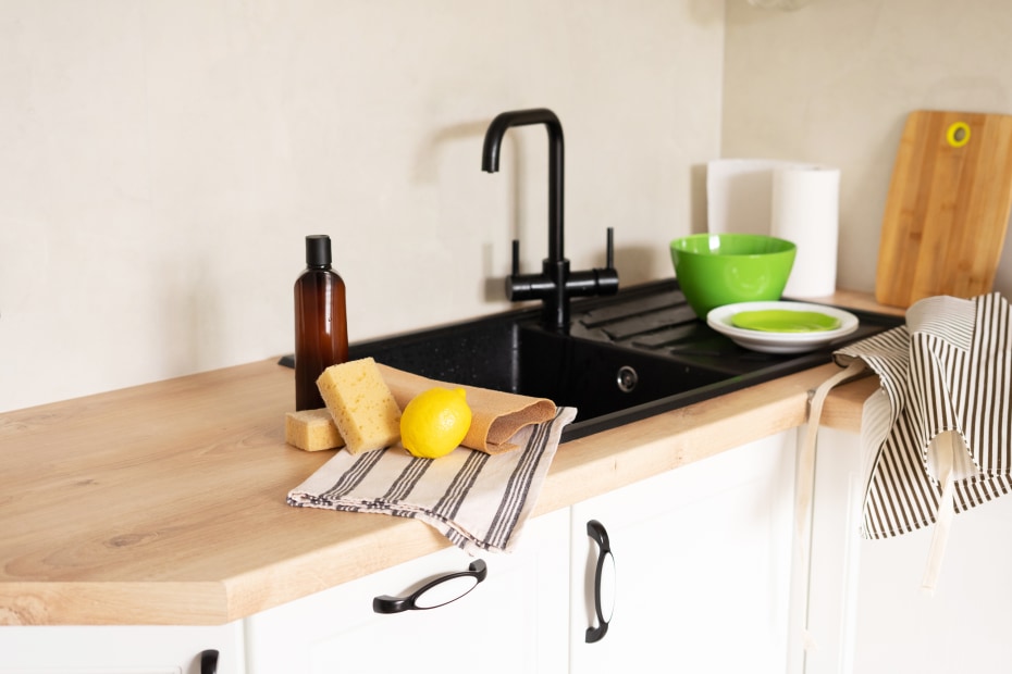 Eco-friendly kitchen supplies sit on the counter next to a modern black kitchen sink and faucet.