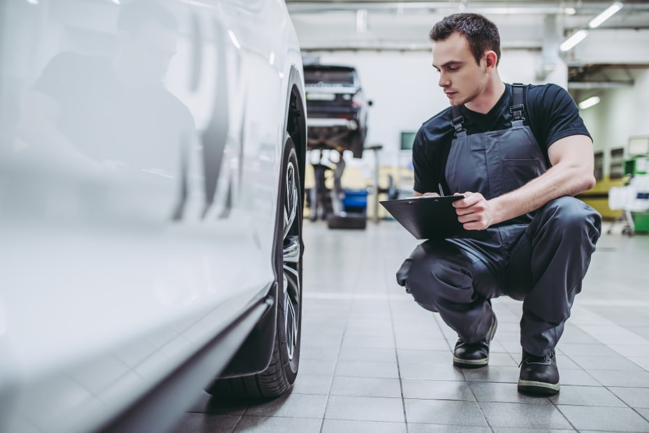 a mechanic looks at checklist while checking the wheels of a car in his shop, picture
