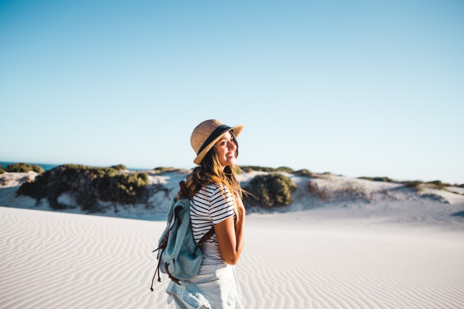 picture of a young woman wearing a backpack with white sand and blue sky in the background