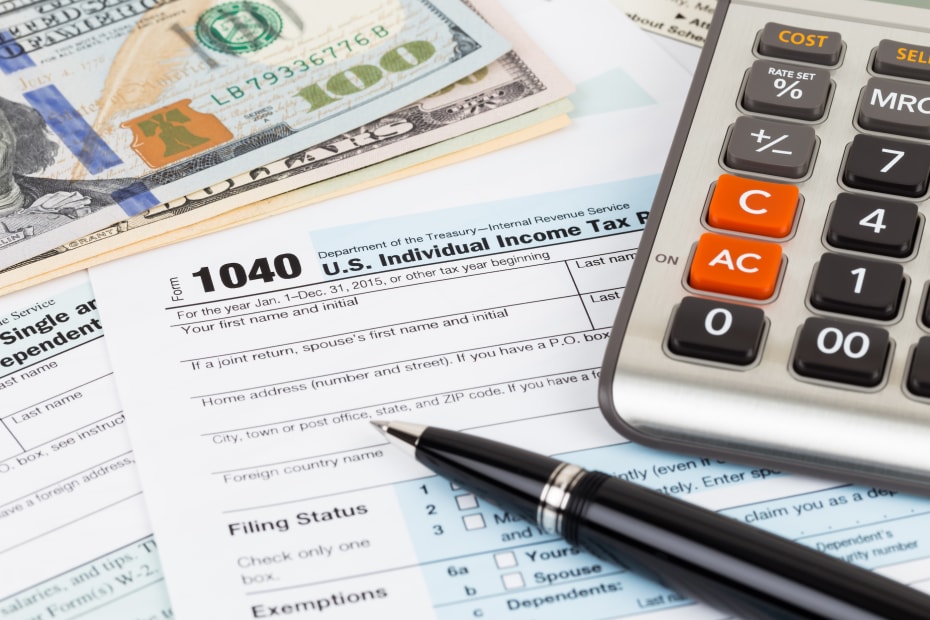 calculator, pen, and cash sitting on top of a 1040 tax form