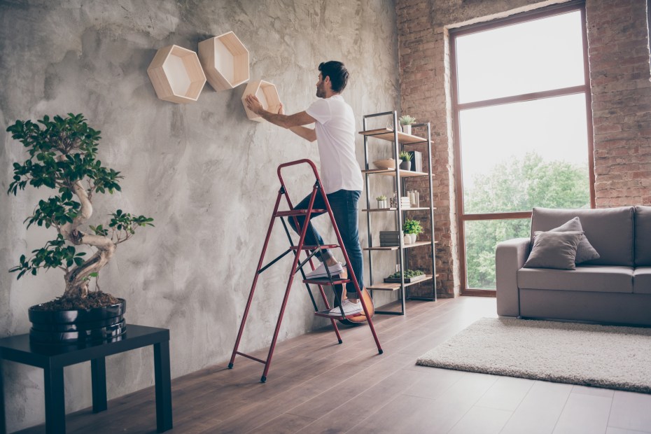 a young man hangs art on the wall of his first apartment