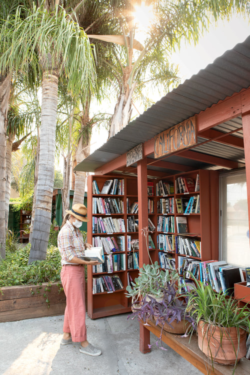 woman wearing straw hat and mask looks at a book from display outside of Bart's Books in Ojai, California.