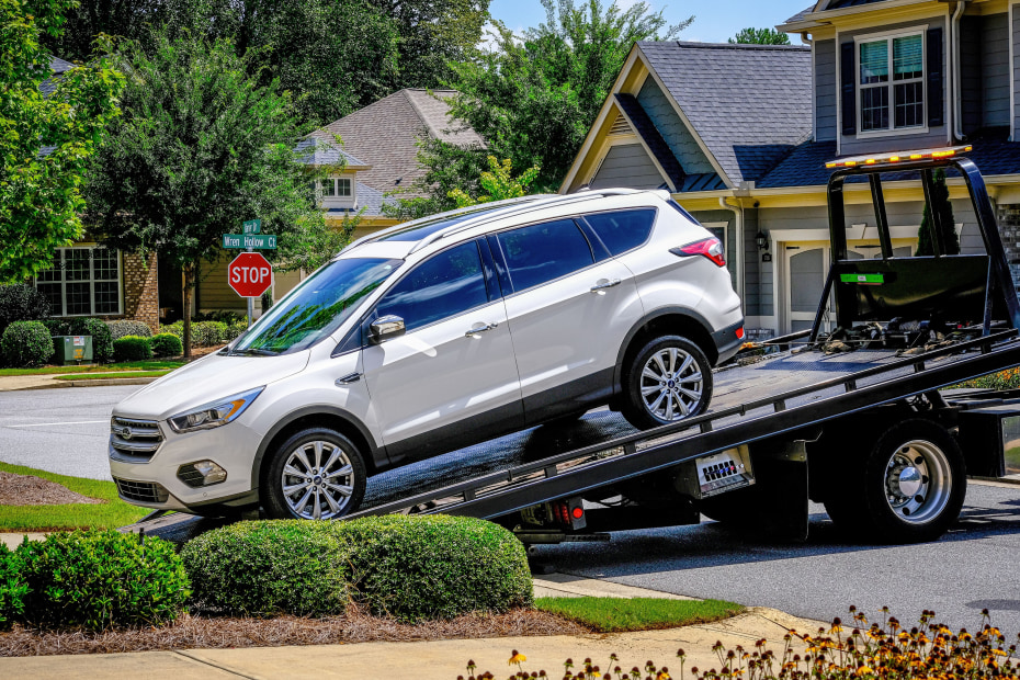 A white SUV is pulled onto a tow truck in a residential neighborhood.