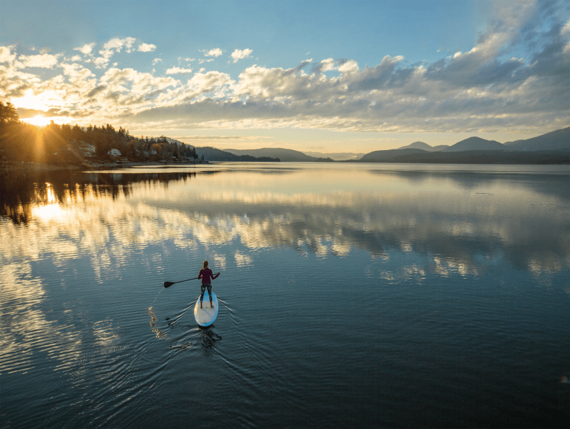 a woman paddleboards across Lake Pend Oreille in Idaho at sunset