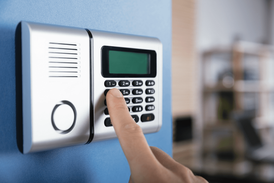 a finger presses the buttons on a home security system mounted to the wall