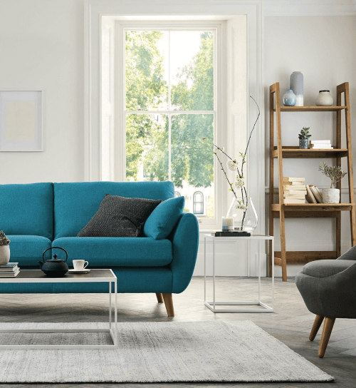teal couch in a bright white living room with pale rug and gray chair