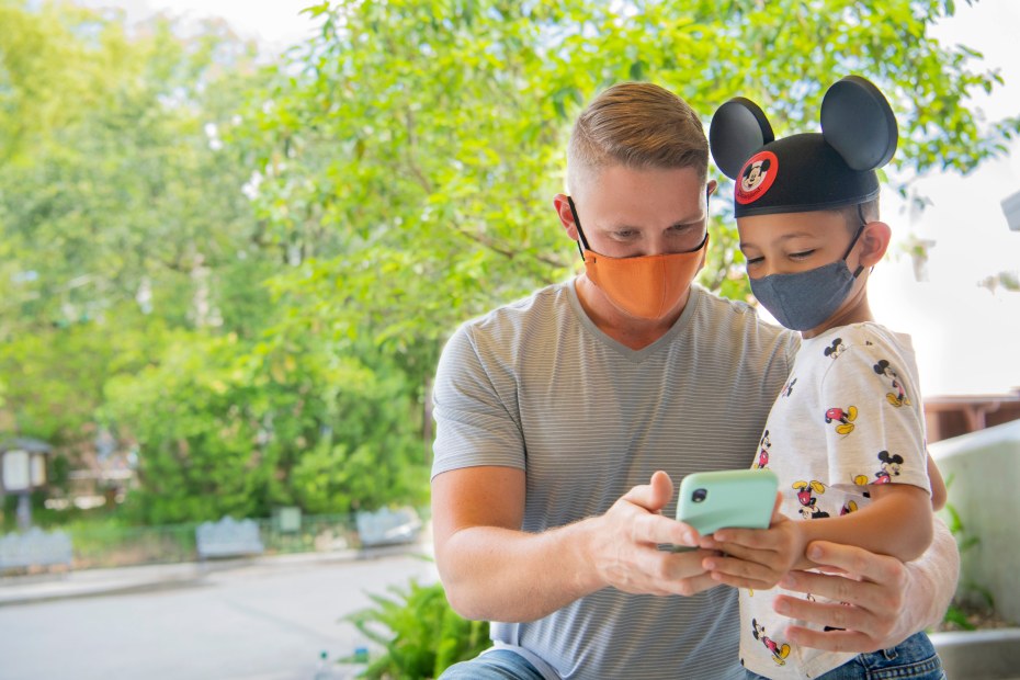 A dad uses the Disneyland App with his son in Disneyland.