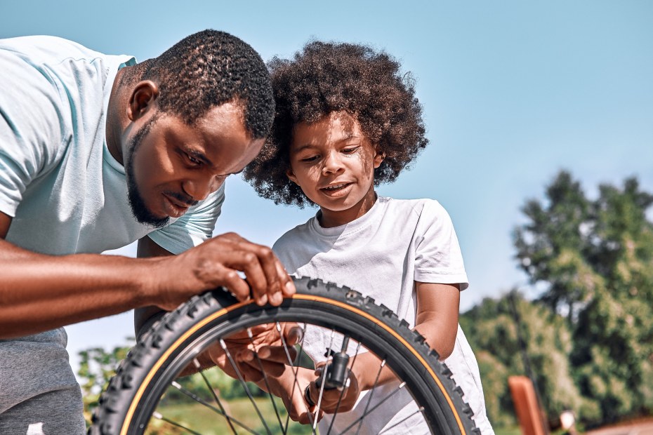 A father and his son pump up the tires on the child's bike.